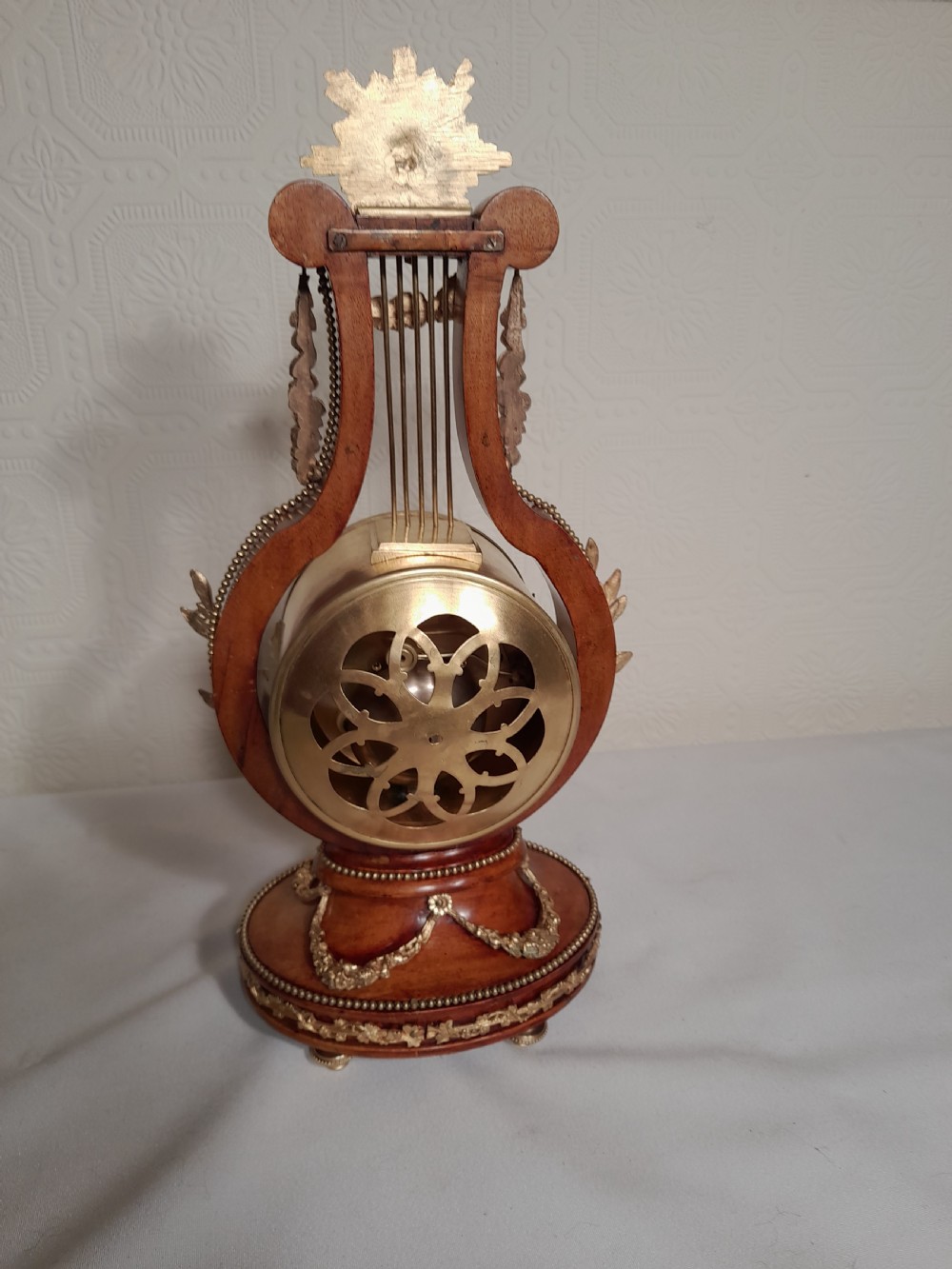 A Louis XVI style wooden lyre clock featuring gilt bronze floral mounts, a sunburst mask finial, and a white enamel dial. View V