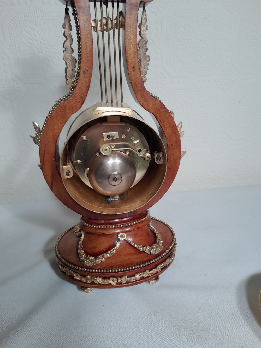 A Louis XVI style wooden lyre clock featuring gilt bronze floral mounts, a sunburst mask finial, and a white enamel dial. View VI