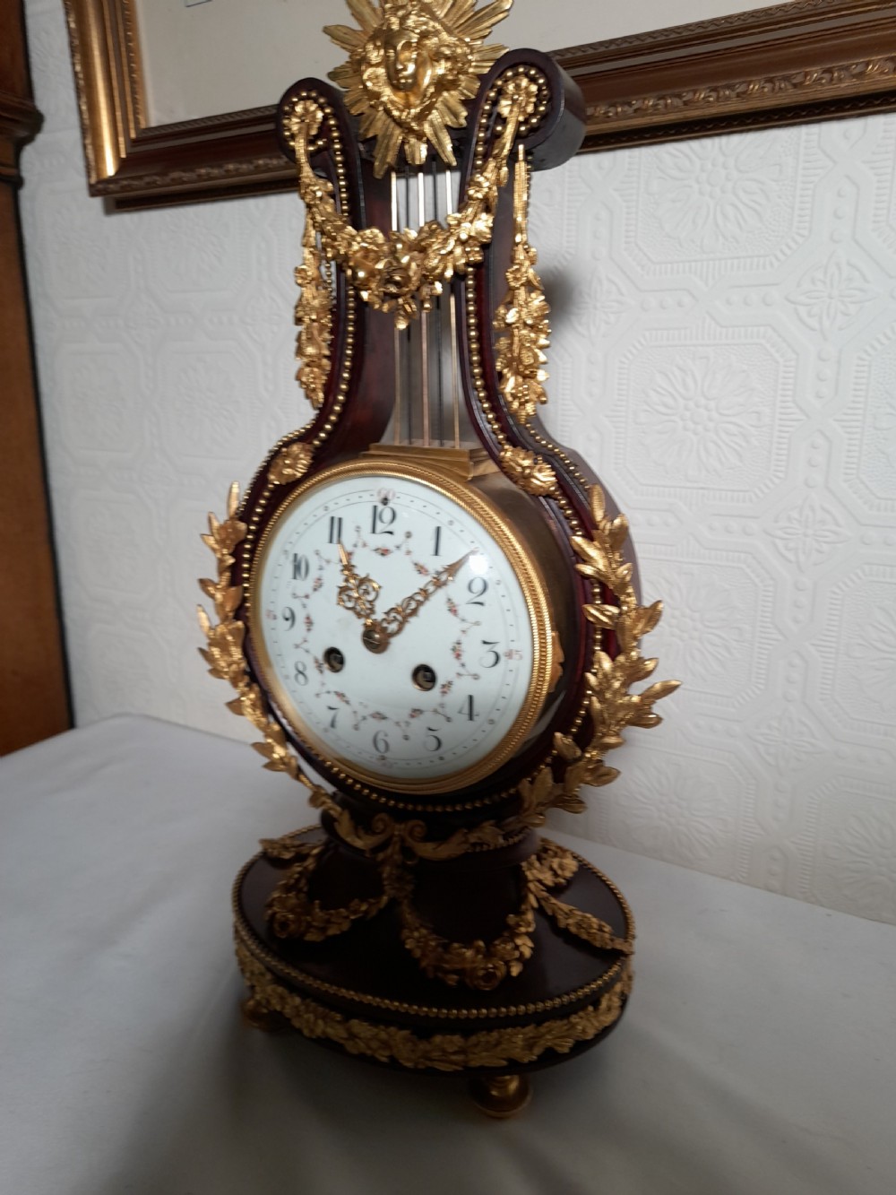A Louis XVI style lyre-shaped mantel clock crafted from dark mahogany with elaborate gilt bronze floral festoons, an Apollo sunburst finial, and a floral enamel dial. View III