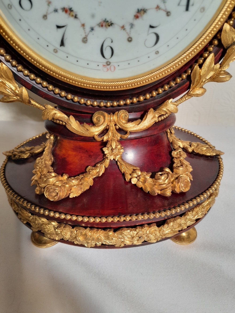 A Louis XVI style lyre-shaped mantel clock crafted from dark mahogany with elaborate gilt bronze floral festoons, an Apollo sunburst finial, and a floral enamel dial. View V