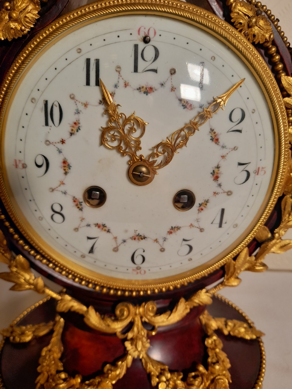 A Louis XVI style lyre-shaped mantel clock crafted from dark mahogany with elaborate gilt bronze floral festoons, an Apollo sunburst finial, and a floral enamel dial. View VI