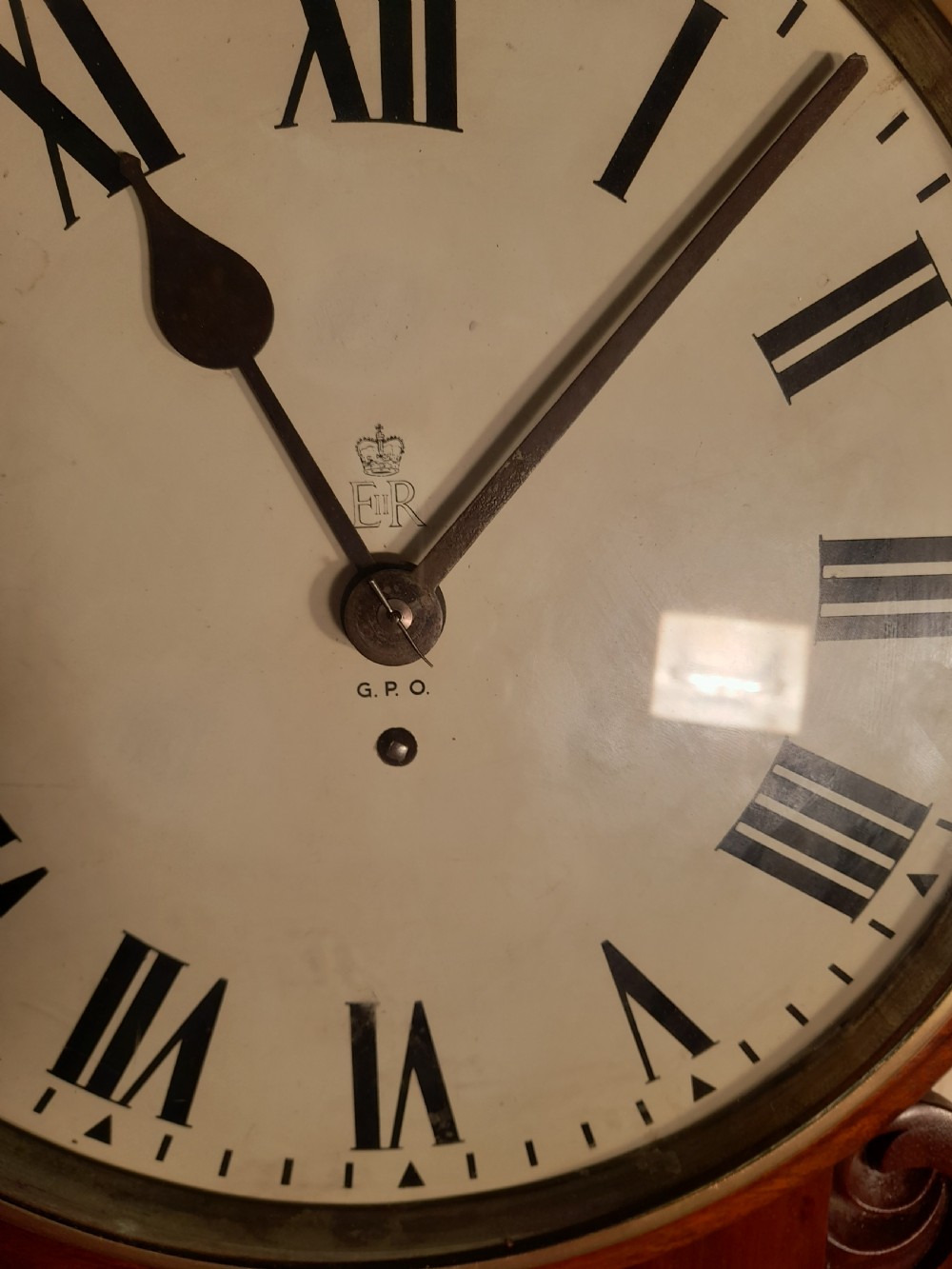An antique mahogany drop dial wall clock featuring an off-white circular dial face with black Roman numerals, a brass bezel, and carved wooden side flourishes. View II