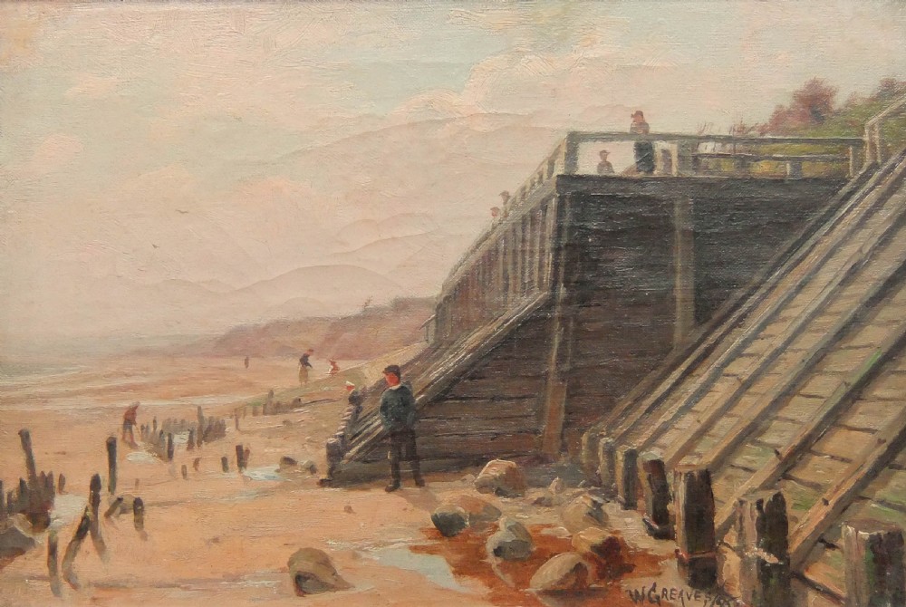 An antique coastal landscape oil painting depicting figures walking along a sandy beach near wooden sea defences and an elevated promenade under a hazy sky, signed by W. Greaves.