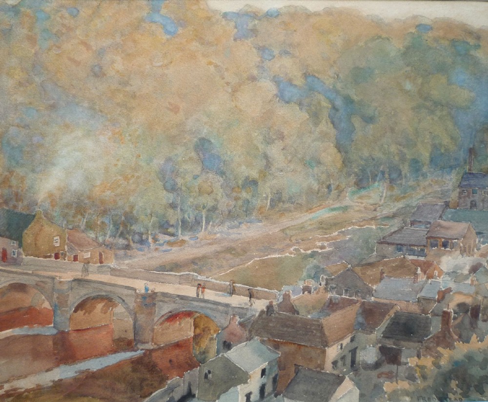 A watercolour painting depicting a stone arch bridge spanning a river alongside town houses and a wooded hillside, signed Fred Stead.