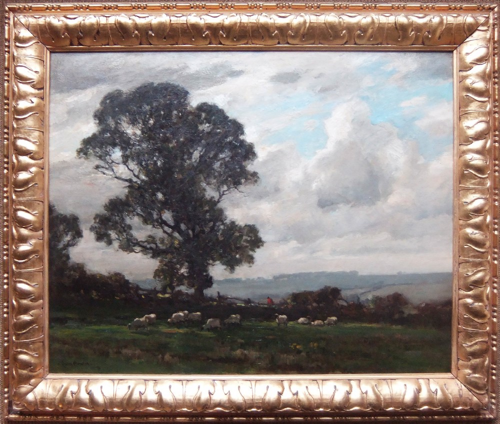 An impressionist landscape oil painting on canvas depicting sheep grazing in a green field under a cloudy sky, set within a carved gilt frame.