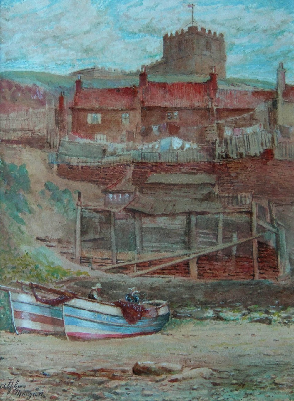 A watercolour painting by Alfred G. Morgan depicting two fishing cobles on a shore in front of brick cottages and a church on a hill in Whitby.