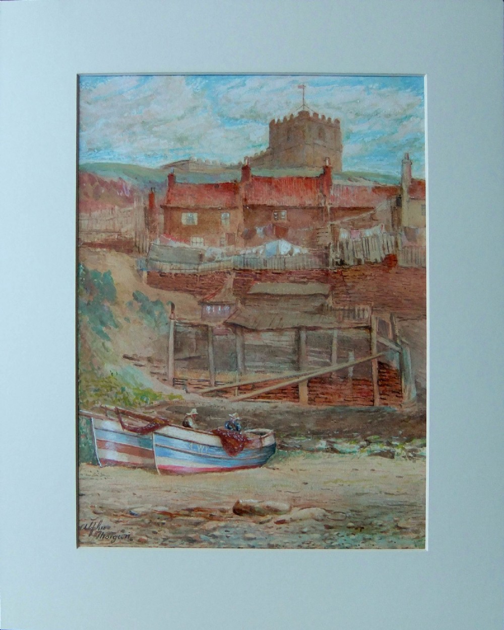 A watercolour painting by Alfred G. Morgan depicting two fishing cobles on a shore in front of brick cottages and a church on a hill in Whitby. View II