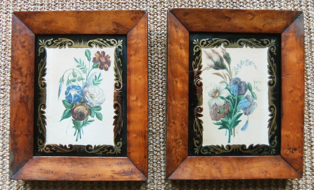 A pair of nineteenth-century botanical watercolour paintings depicting floral sprays, encased in wide birds eye maple frames with black and gold decorative glass borders.