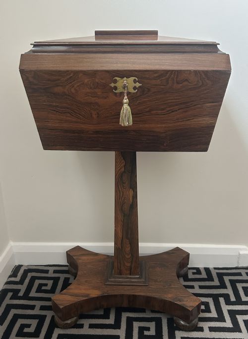fig 1. A Regency rosewood teapoy featuring a sarcophagus-shaped caddy top, brass escutcheon with key and tassel, set upon a central column and a four-pointed concave base.