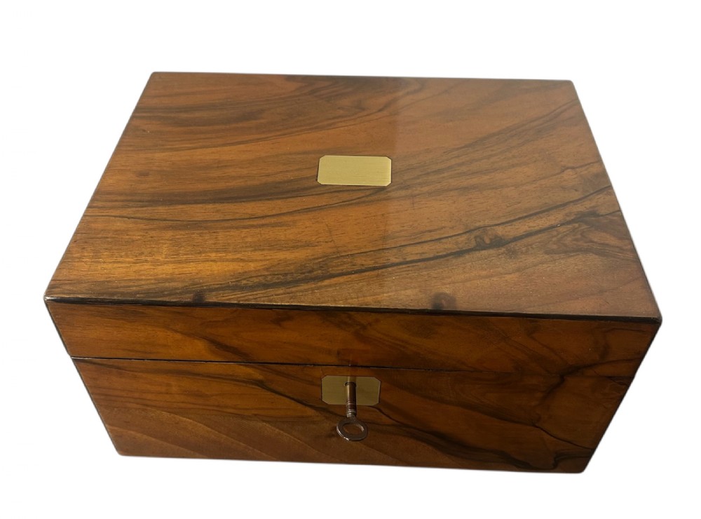 A rectangular warm brown figured walnut box featuring a brass cartouche on the lid and a brass escutcheon with a key.