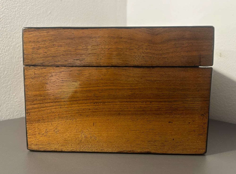 A rectangular warm brown figured walnut box featuring a brass cartouche on the lid and a brass escutcheon with a key. View V