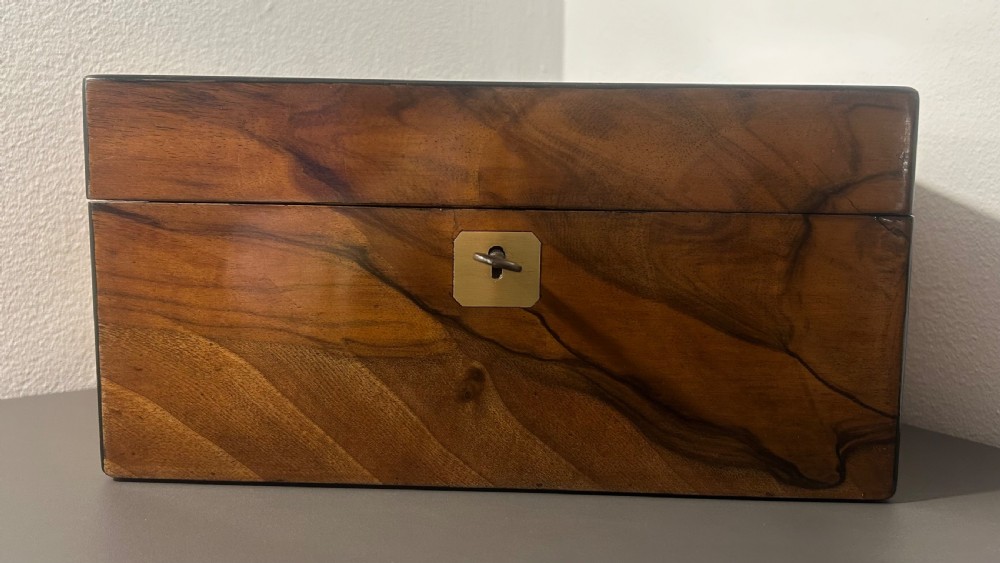 A rectangular warm brown figured walnut box featuring a brass cartouche on the lid and a brass escutcheon with a key. View VI