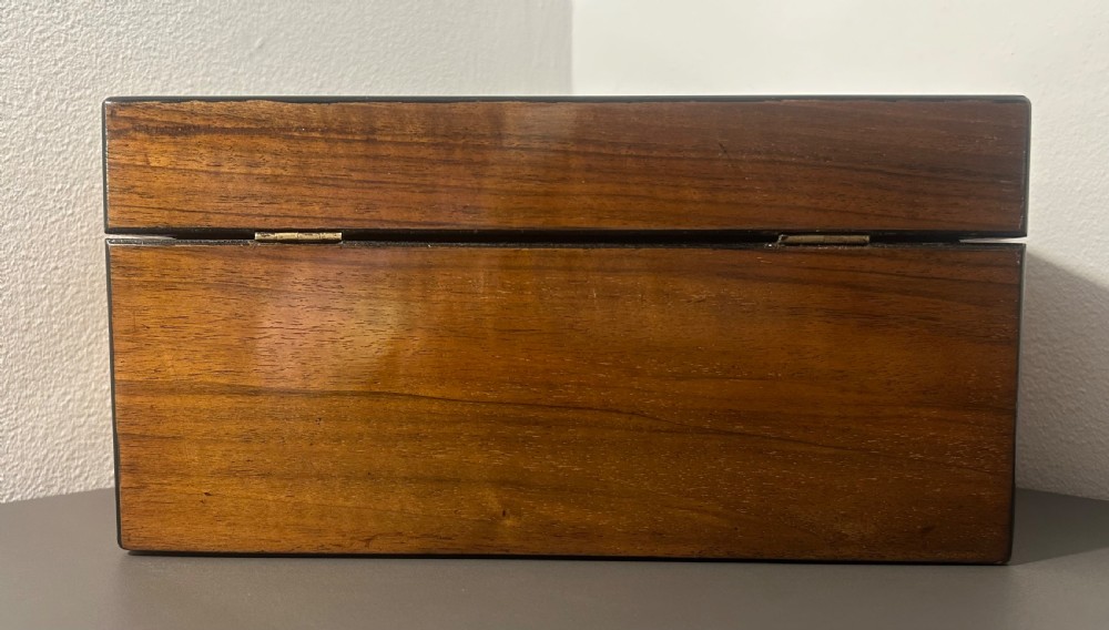 A rectangular warm brown figured walnut box featuring a brass cartouche on the lid and a brass escutcheon with a key. View VII