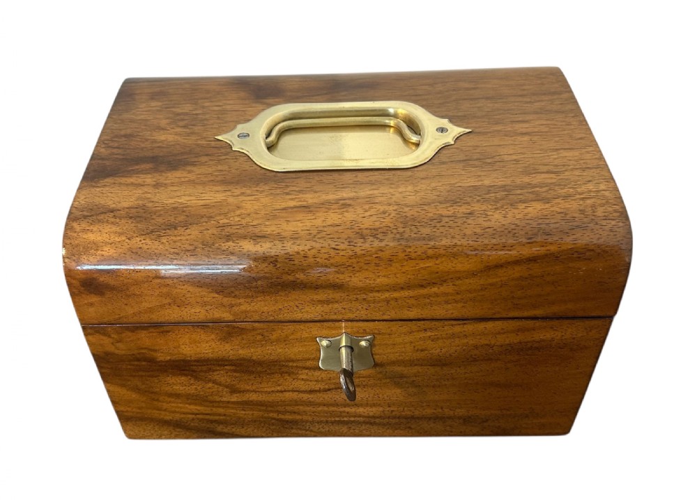 A Victorian warm brown walnut jewellery box featuring a domed lid, inset brass handle, and a brass key inserted into the front escutcheon.