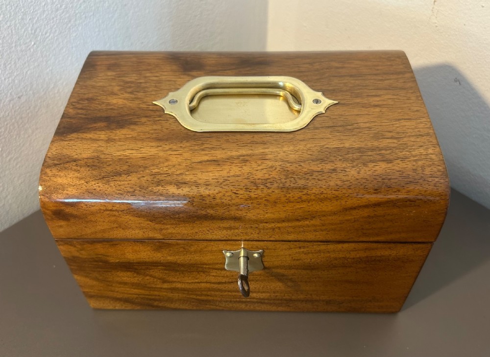 A Victorian warm brown walnut jewellery box featuring a domed lid, inset brass handle, and a brass key inserted into the front escutcheon. View IV