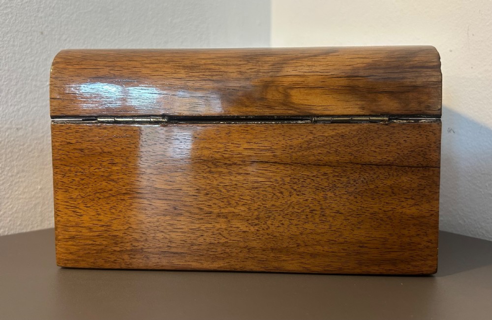 A Victorian warm brown walnut jewellery box featuring a domed lid, inset brass handle, and a brass key inserted into the front escutcheon. View VI