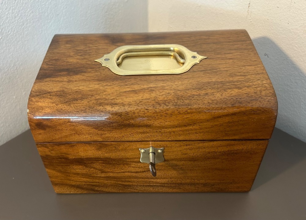 A Victorian warm brown walnut jewellery box featuring a domed lid, inset brass handle, and a brass key inserted into the front escutcheon. View VIII