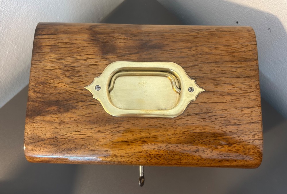 A Victorian warm brown walnut jewellery box featuring a domed lid, inset brass handle, and a brass key inserted into the front escutcheon. View X