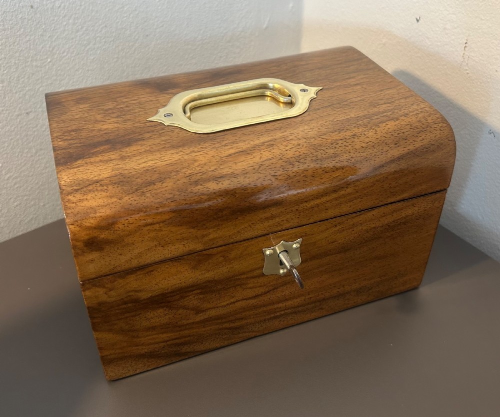 A Victorian warm brown walnut jewellery box featuring a domed lid, inset brass handle, and a brass key inserted into the front escutcheon. View XI