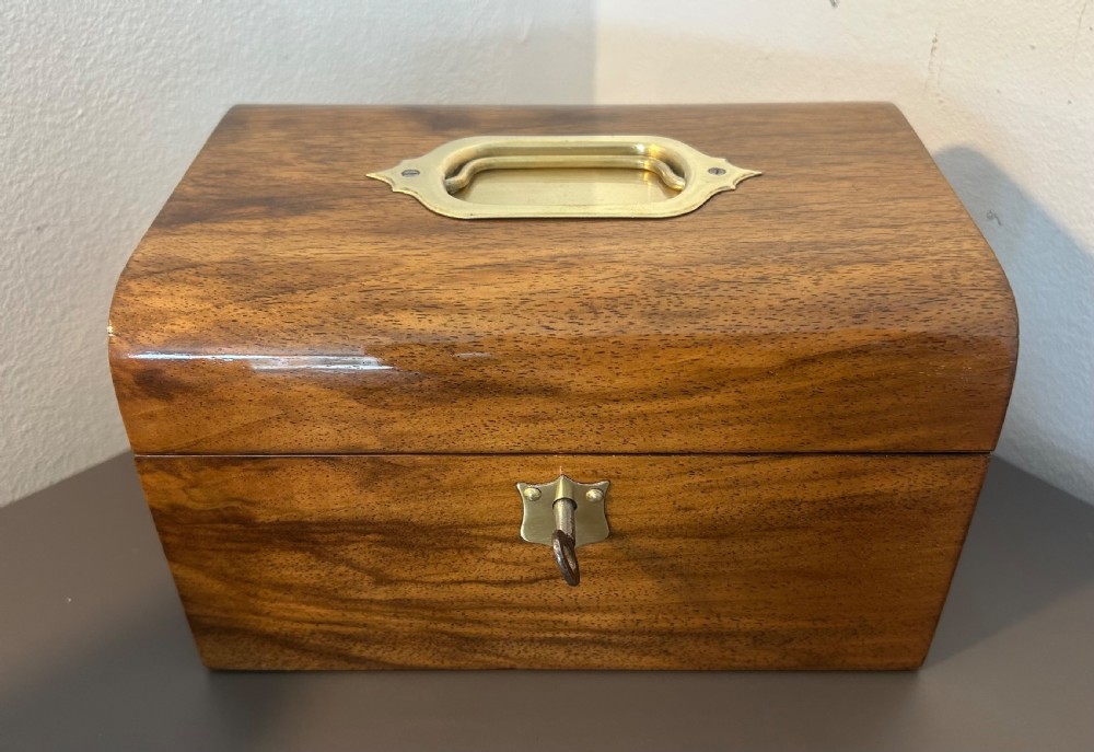 A Victorian warm brown walnut jewellery box featuring a domed lid, inset brass handle, and a brass key inserted into the front escutcheon. View XIV