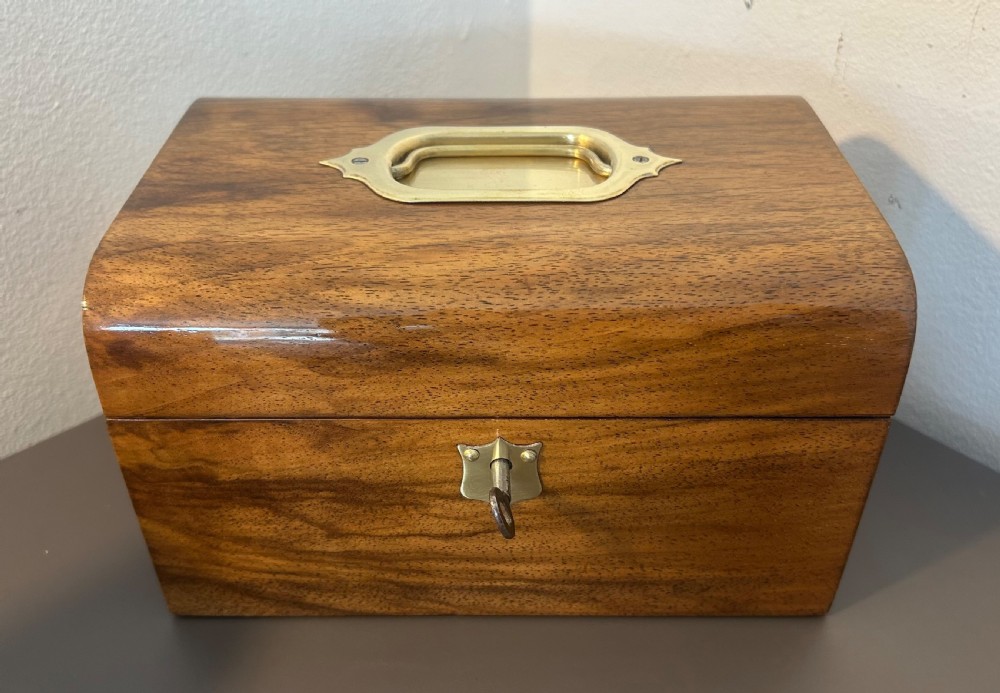 A Victorian warm brown walnut jewellery box featuring a domed lid, inset brass handle, and a brass key inserted into the front escutcheon. View XV