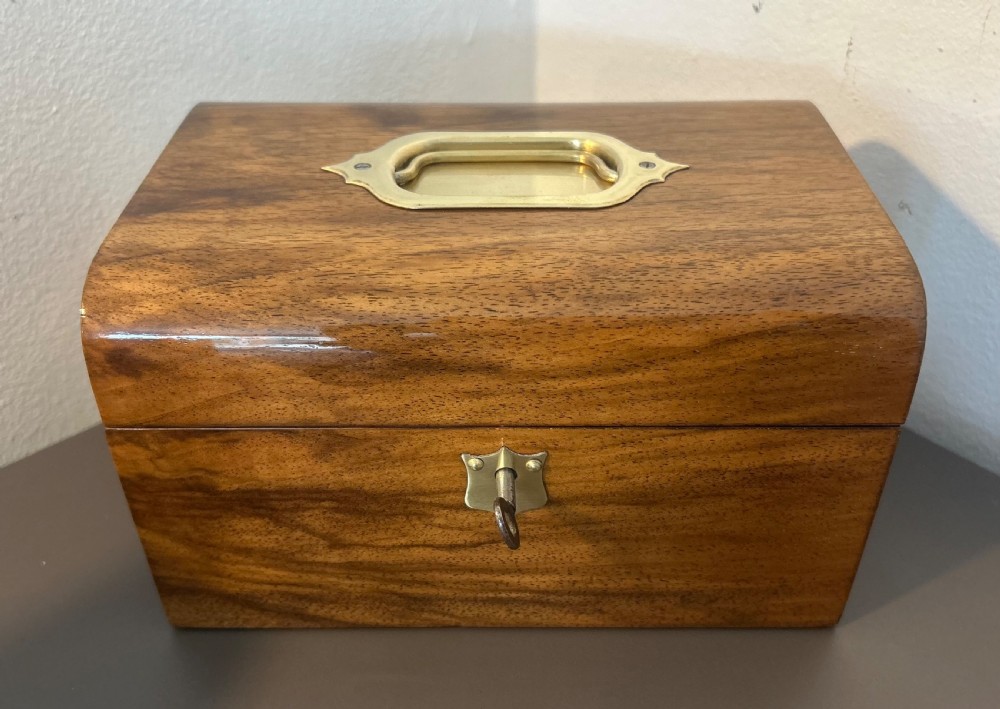 A Victorian warm brown walnut jewellery box featuring a domed lid, inset brass handle, and a brass key inserted into the front escutcheon. View XVI
