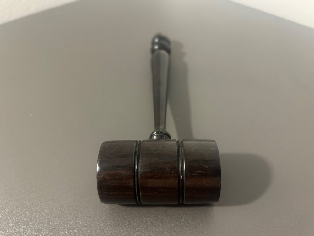 A turned dark ebony wood gavel featuring a cylindrical head with incised ring details and a lathe-turned handle ending in a rounded finial. View II