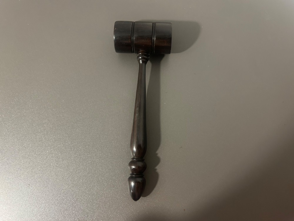 A turned dark ebony wood gavel featuring a cylindrical head with incised ring details and a lathe-turned handle ending in a rounded finial. View III
