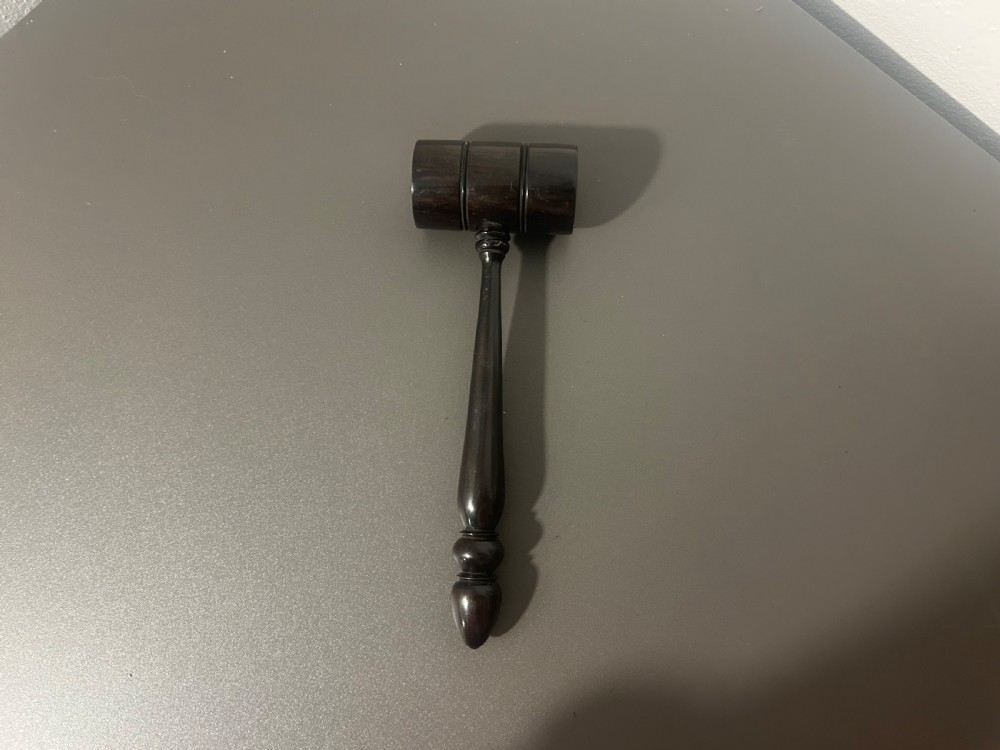 A turned dark ebony wood gavel featuring a cylindrical head with incised ring details and a lathe-turned handle ending in a rounded finial. View IV