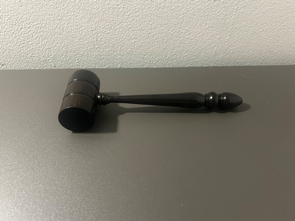 A turned dark ebony wood gavel featuring a cylindrical head with incised ring details and a lathe-turned handle ending in a rounded finial. View VII
