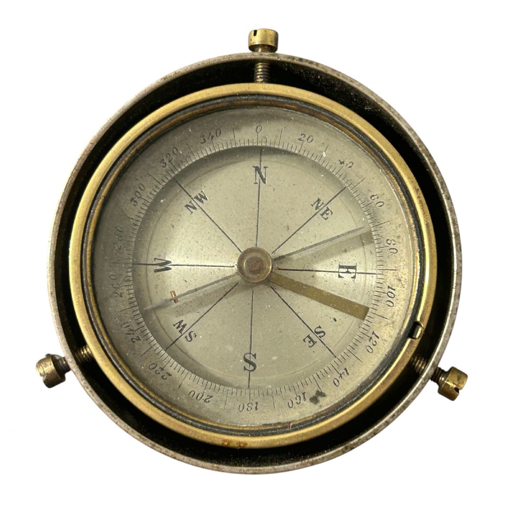 A circular Victorian brass table compass featuring a glass bezel, engraved directional dial, and an outer brass ring with threaded screws.