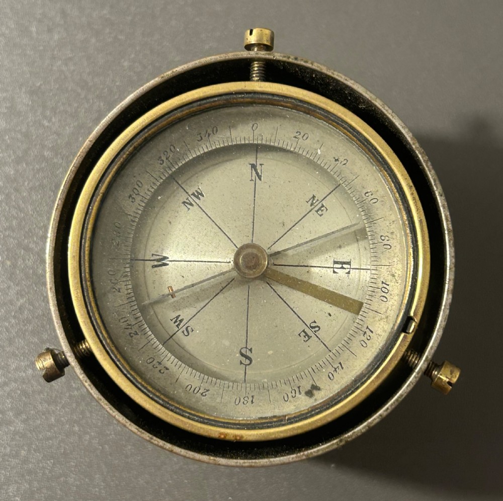 A circular Victorian brass table compass featuring a glass bezel, engraved directional dial, and an outer brass ring with threaded screws. View II