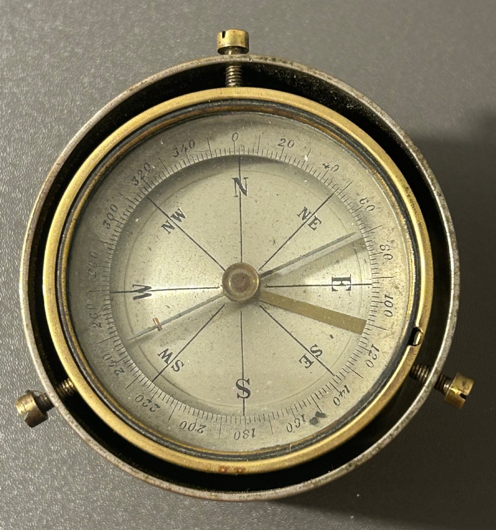 A circular Victorian brass table compass featuring a glass bezel, engraved directional dial, and an outer brass ring with threaded screws. View III