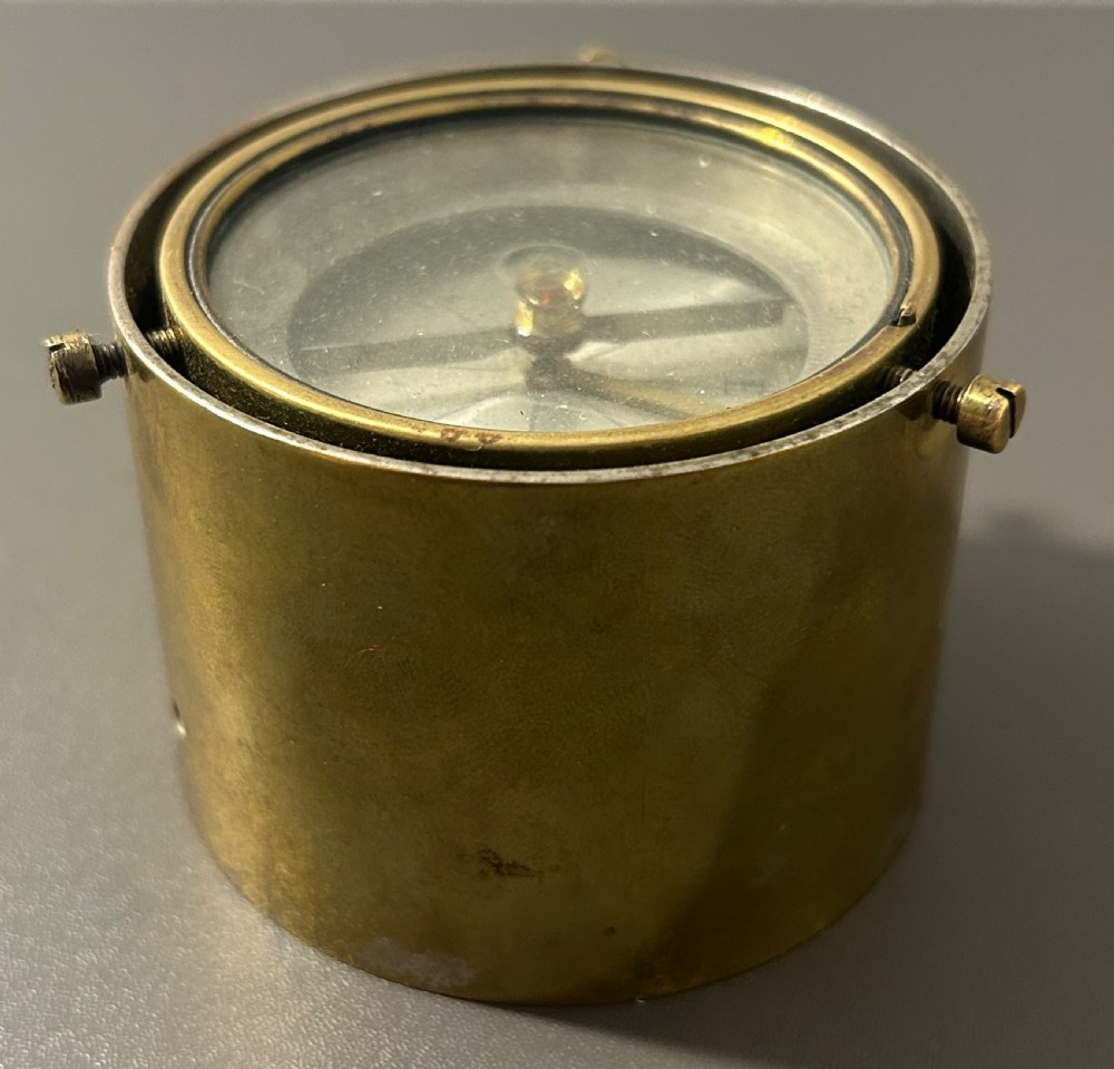 A circular Victorian brass table compass featuring a glass bezel, engraved directional dial, and an outer brass ring with threaded screws. View V
