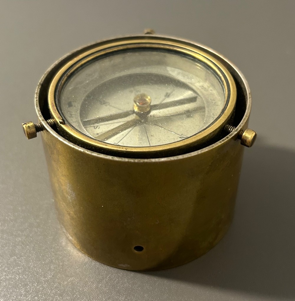 A circular Victorian brass table compass featuring a glass bezel, engraved directional dial, and an outer brass ring with threaded screws. View VI