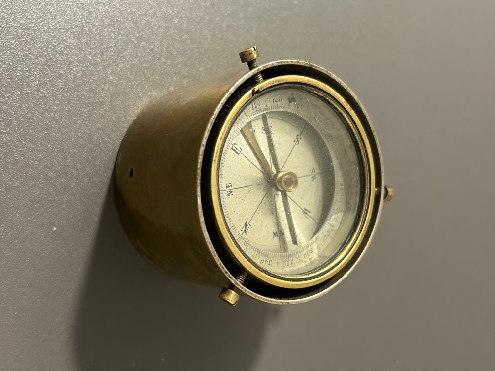A circular Victorian brass table compass featuring a glass bezel, engraved directional dial, and an outer brass ring with threaded screws. View VII