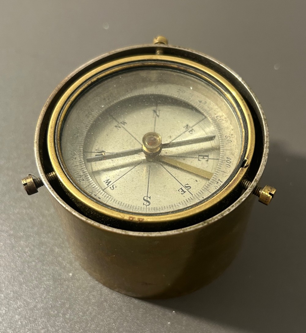 A circular Victorian brass table compass featuring a glass bezel, engraved directional dial, and an outer brass ring with threaded screws. View VIII