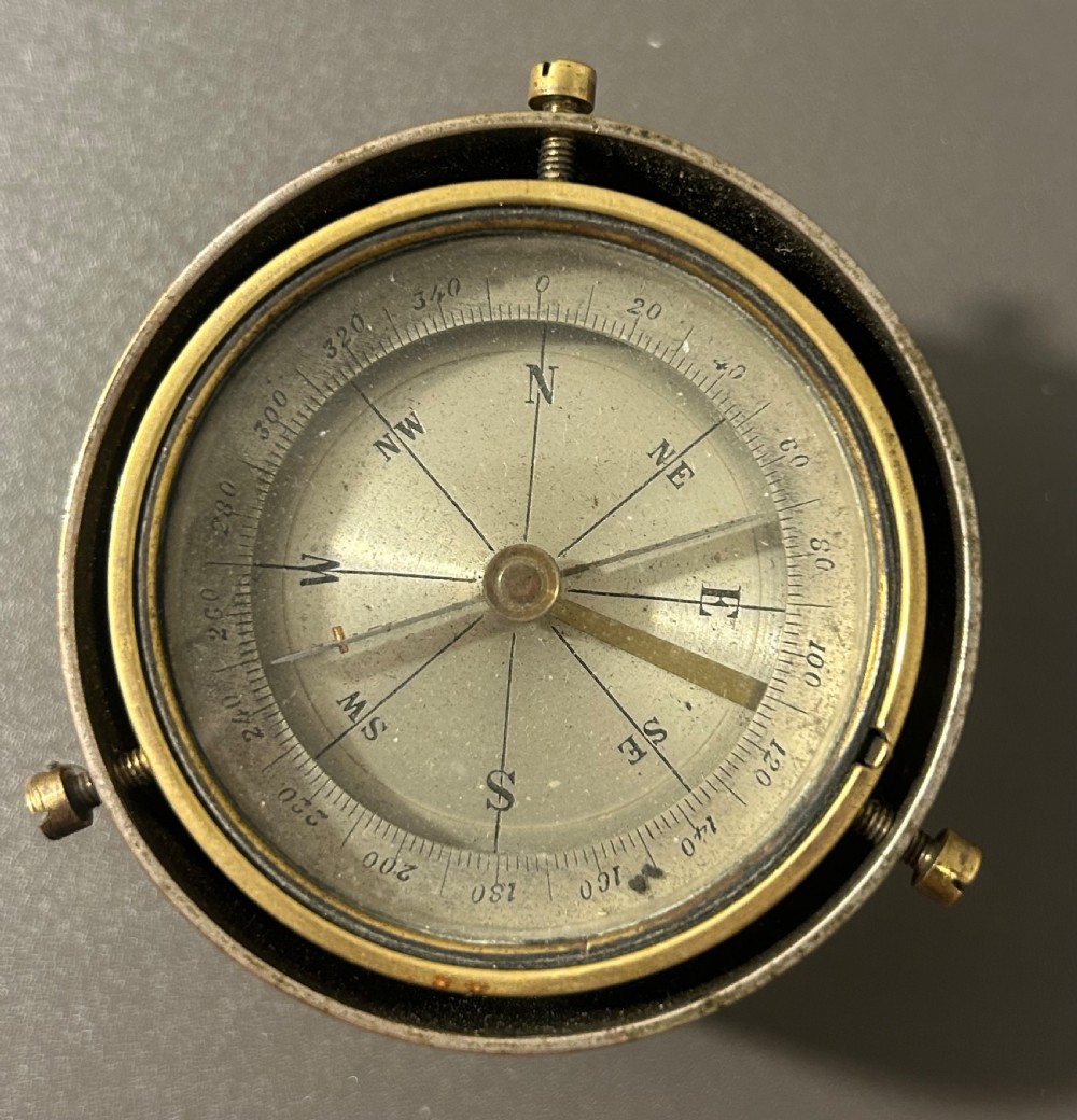 A circular Victorian brass table compass featuring a glass bezel, engraved directional dial, and an outer brass ring with threaded screws. View IX