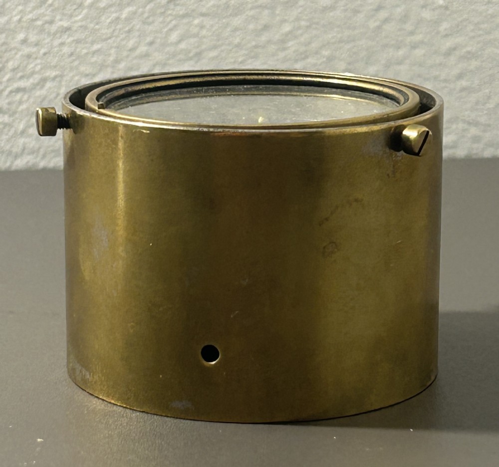 A circular Victorian brass table compass featuring a glass bezel, engraved directional dial, and an outer brass ring with threaded screws. View XI