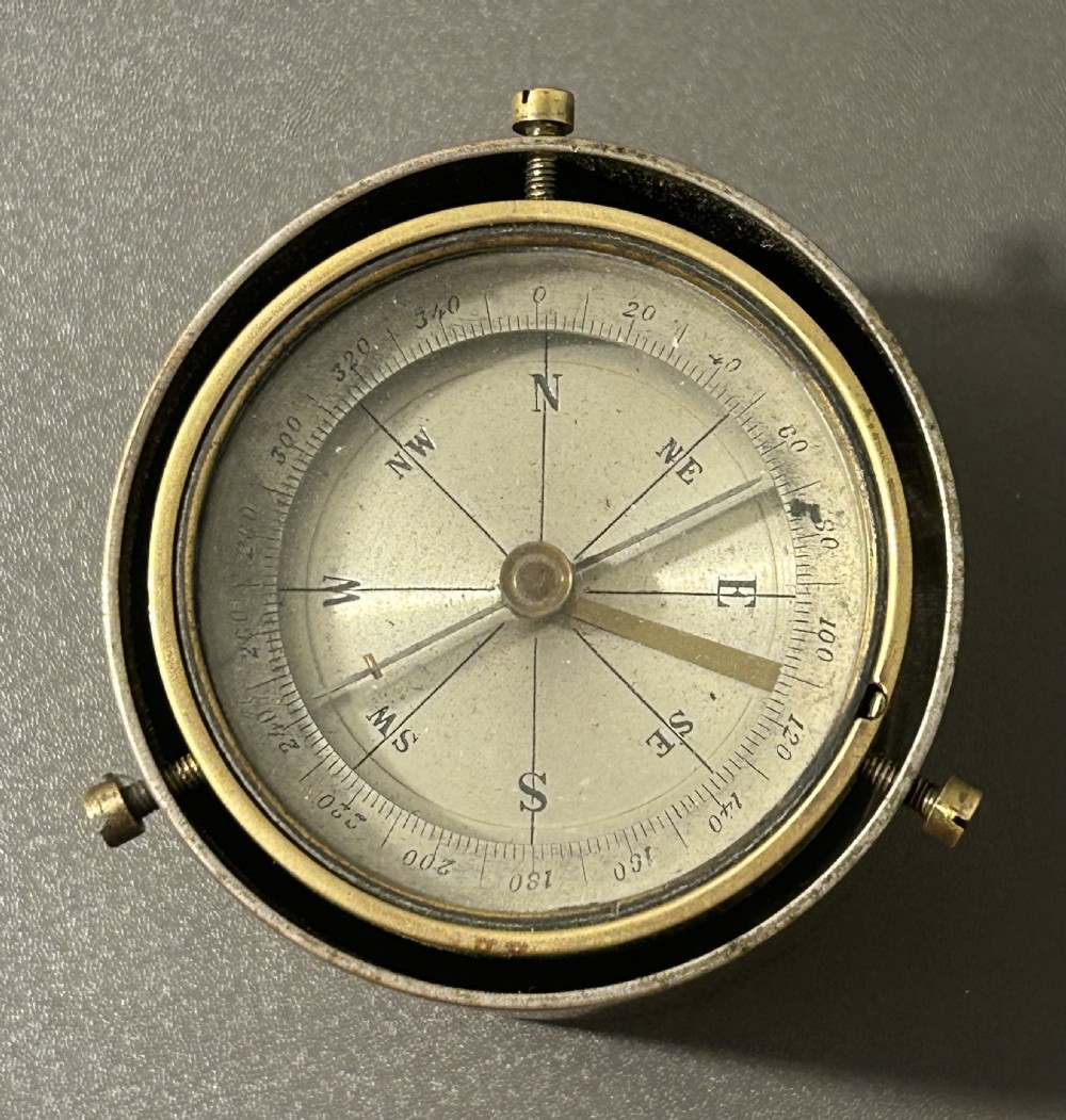 A circular Victorian brass table compass featuring a glass bezel, engraved directional dial, and an outer brass ring with threaded screws. View XV