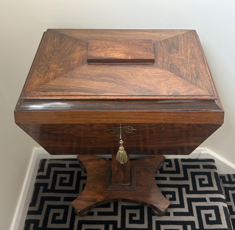 A Regency rosewood teapoy featuring a sarcophagus-shaped caddy top, brass escutcheon with key and tassel, set upon a central column and a four-pointed concave base. View VII