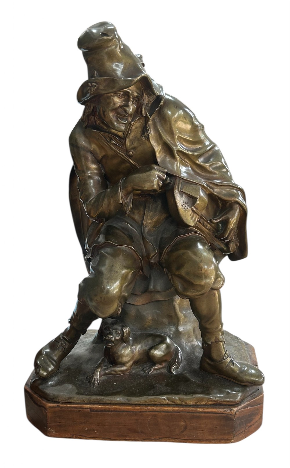 A patinated dark bronze sculpture depicting a seated male musician with a hurdy-gurdy instrument and a small dog at his feet on a wooden plinth.