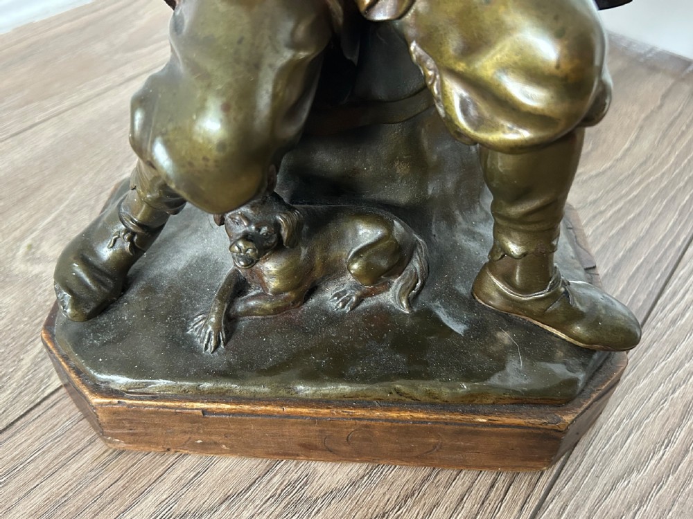 A patinated dark bronze sculpture depicting a seated male musician with a hurdy-gurdy instrument and a small dog at his feet on a wooden plinth. View VI