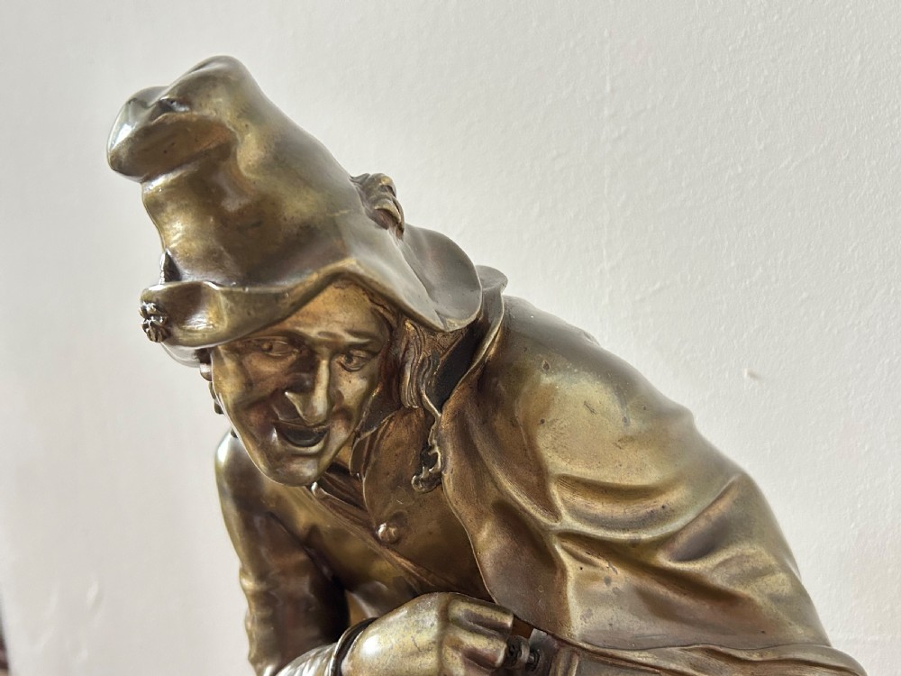 A patinated dark bronze sculpture depicting a seated male musician with a hurdy-gurdy instrument and a small dog at his feet on a wooden plinth. View X