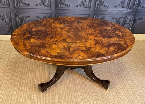 fig 2. An oval Victorian low coffee table featuring a bookmatched burr walnut veneer top supported by dark curved legs on small castors.