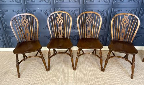 fig 1. A set of four warm brown wooden Windsor style dining chairs with hoop backs, pierced central splats, and turned legs.