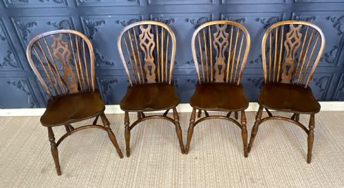 fig 2. A set of four warm brown wooden Windsor style dining chairs with hoop backs, pierced central splats, and turned legs.