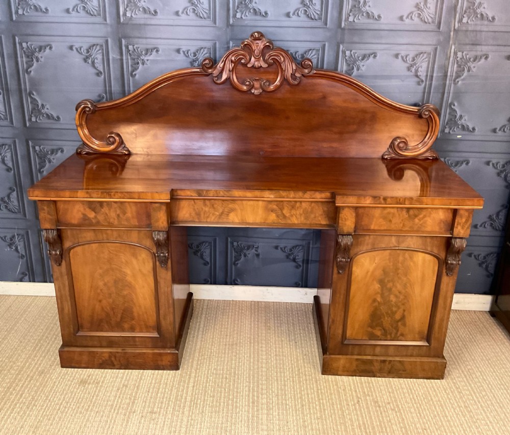 A Victorian mahogany pedestal sideboard featuring a carved arched backboard, flame mahogany veneer panels, and twin pedestal cupboards. View II