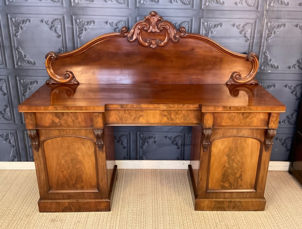 A Victorian mahogany pedestal sideboard featuring a carved arched backboard, flame mahogany veneer panels, and twin pedestal cupboards. View III