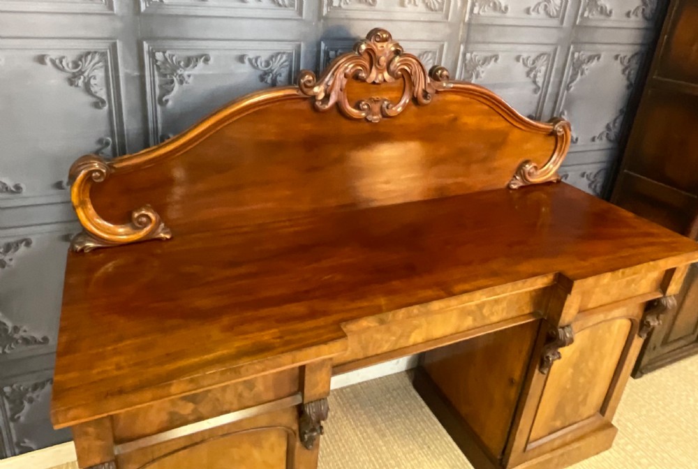 A Victorian mahogany pedestal sideboard featuring a carved arched backboard, flame mahogany veneer panels, and twin pedestal cupboards. View IV